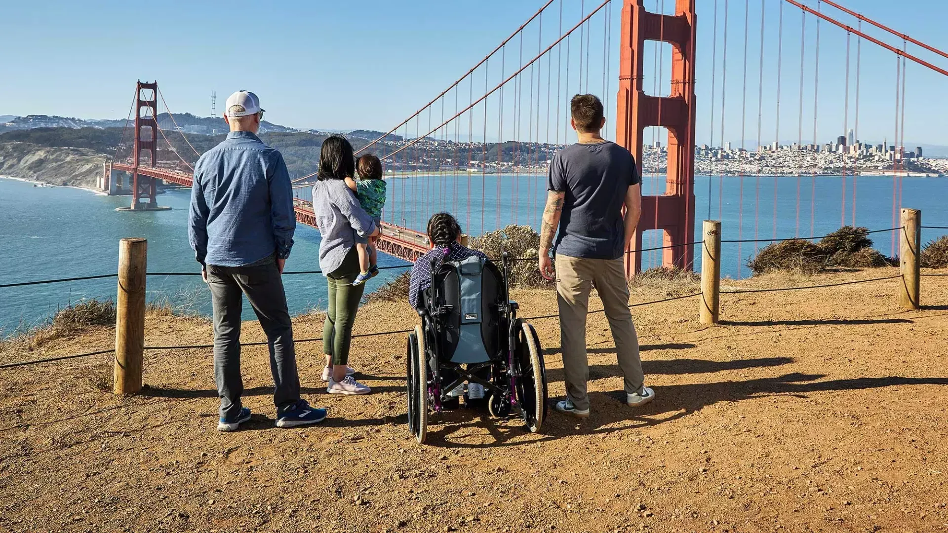 一群人, 包括一个坐轮椅的人, é visto por trás enquanto olham para a 金门大桥 de Marin Headlands.