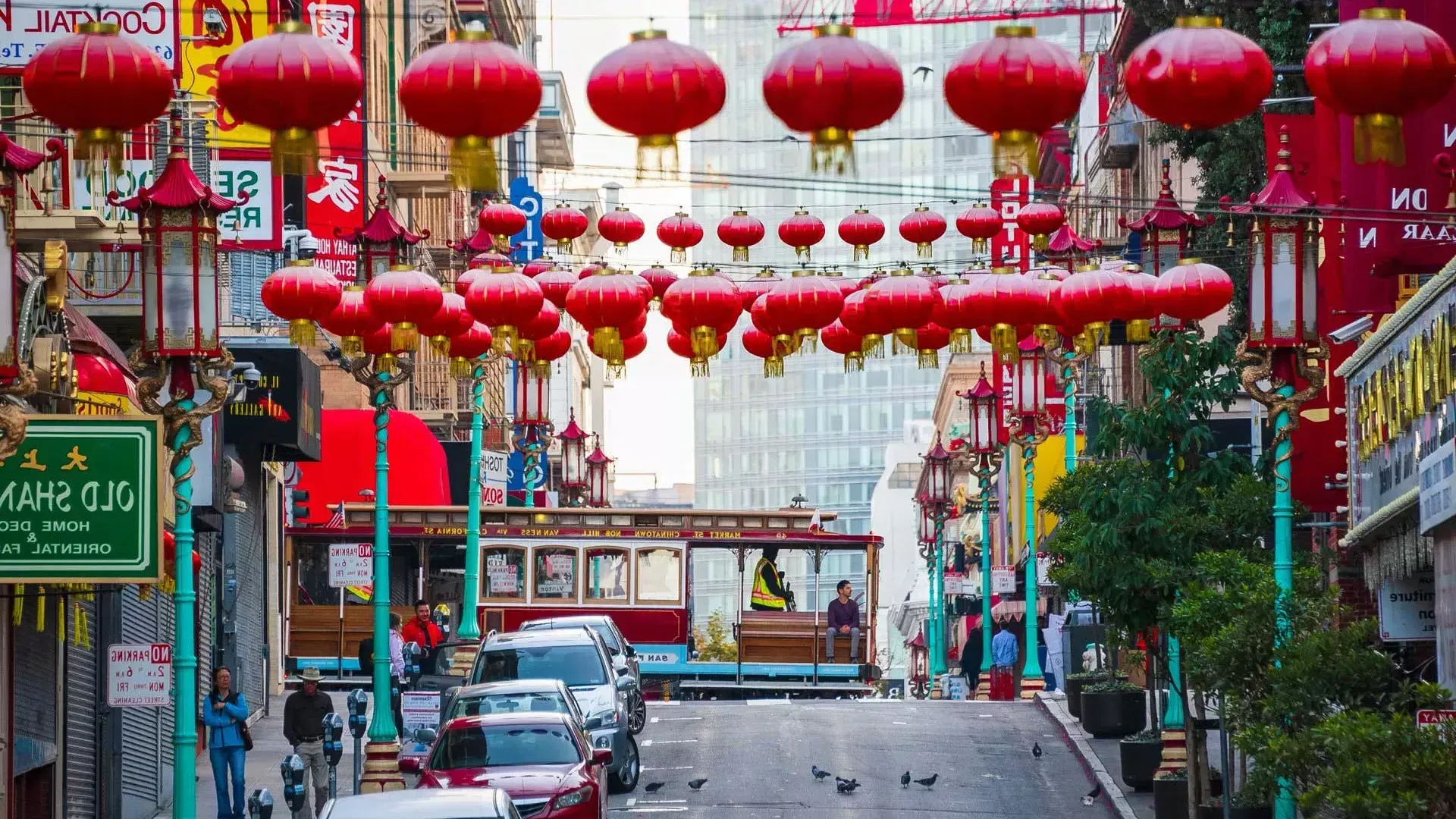 Abgebildet ist eine hügelige Straße in San Franciscos Chinatown mit baumelnden roten Laternen und einer vorbeifahrenden Straßenbahn.