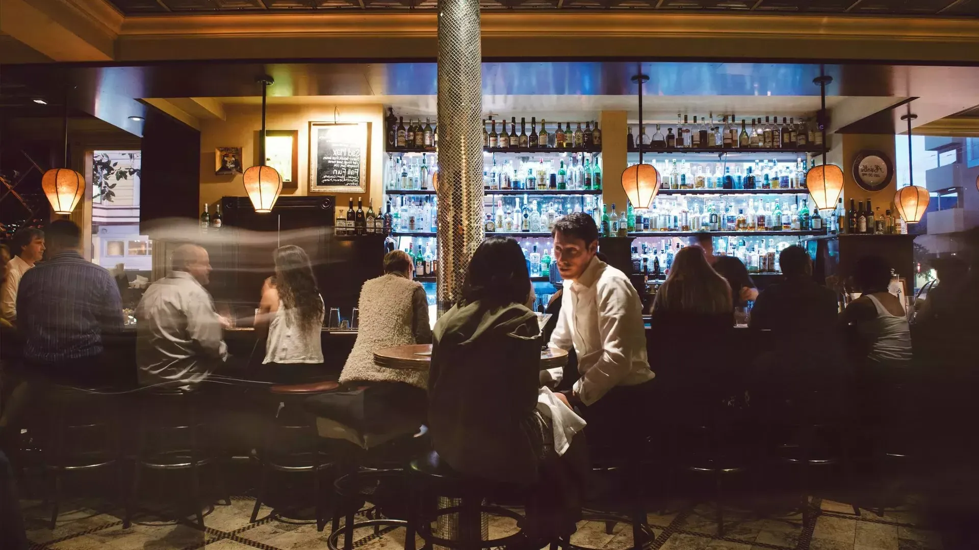 A couple share drinks at a busy San Francisco bar.