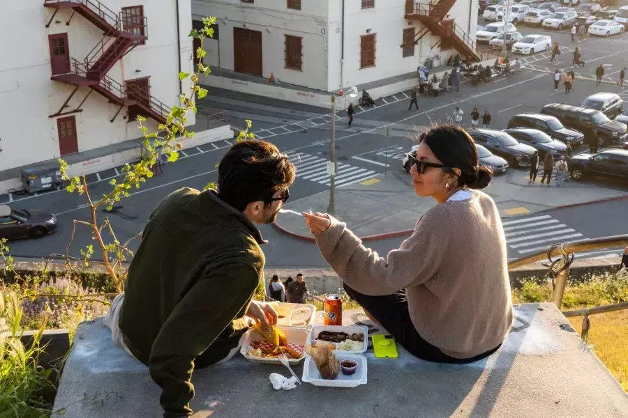 Un couple dîne en plein air au Fort Mason Center de 贝博体彩app. La femme donne à son compagnon un avant-goût de la nourriture.