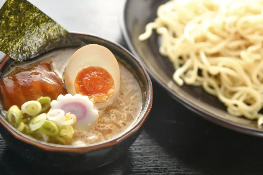 麺とラーメンスープのボウル、そして半分に切ったポーチドエッグのクローズアップショット。