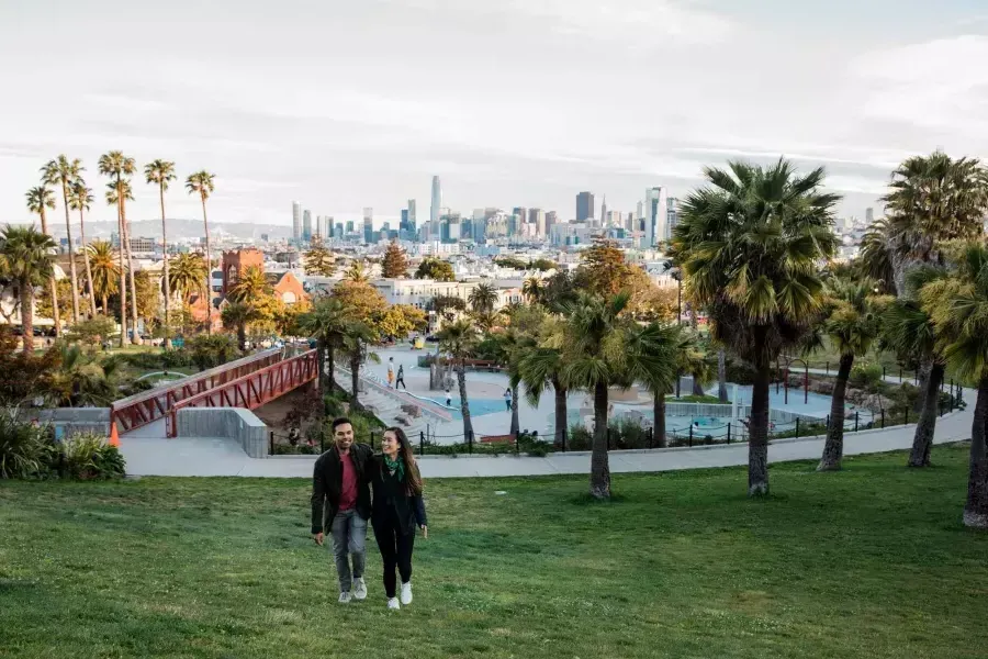 Un couple se dirige vers la caméra avec Dolores Park et la Skyline de 贝博体彩app derrière eux.