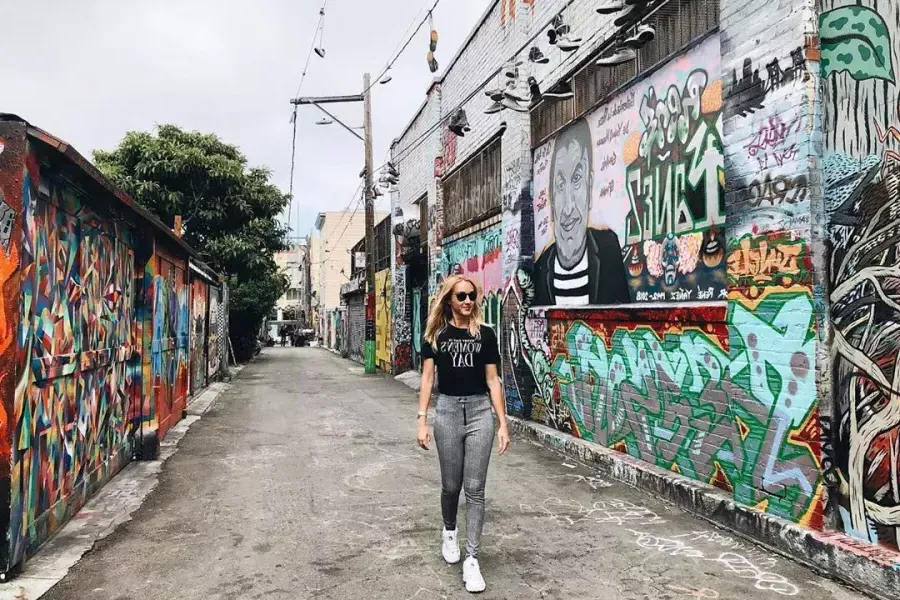 A woman walks through an alley in the 任务的区 that is covered with murals and artwork. 贝博体彩app，加利福尼亚.