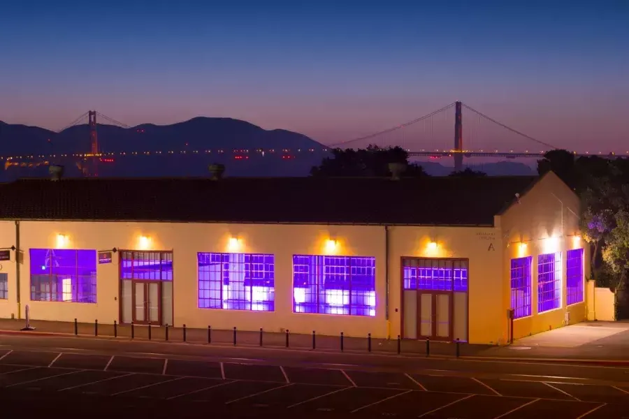 Das Fort Mason-Gebäude wird nachts mit einer violetten Innenbeleuchtung beleuchtet, 背景是桥.