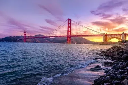 Le 金门大桥 au coucher du soleil avec un ciel multicolore et la baie de San Francisco au premier plan.