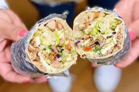 Un burrito de style mission, 用铝箔包裹，切成两半, est montré à la caméra.